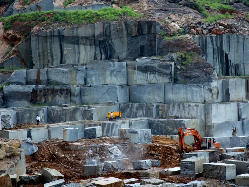 A quarry foreman calculating block dimensions and marking pushing bag insertion points on a massive cut granite block